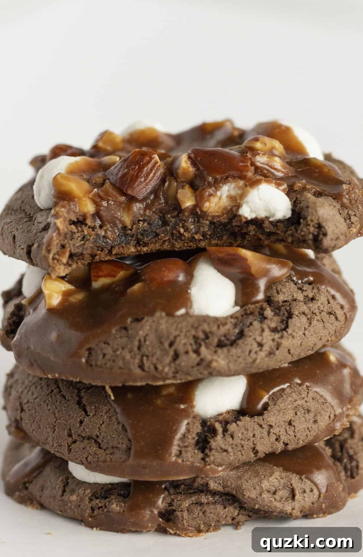 A perfectly composed stack of four fudgy Rocky Road Cookies, showcasing their rich chocolate, melted marshmallows, and glistening almond-flecked frosting.
