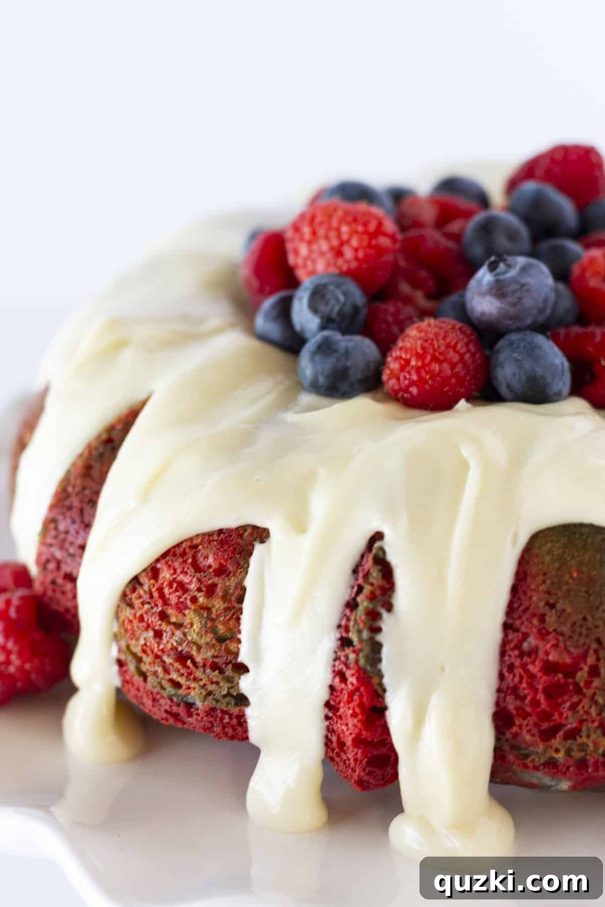 Easy Patriotic Burst Bundt 7 A beautifully completed firecracker bundt cake, garnished with fresh blueberries and raspberries in the center, showcased on a cake stand.