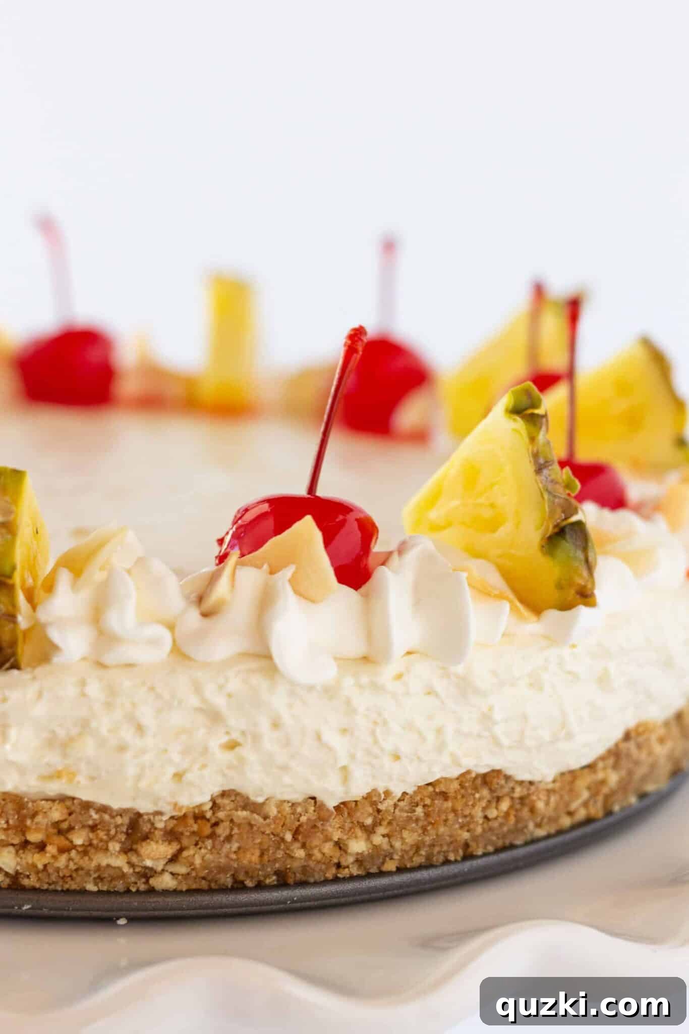 Island Escape No-Bake Cheesecake 2 A vibrant no-bake Pina Colada Cheesecake, garnished generously with fresh pineapple wedges and bright red maraschino cherries, ready to be served.