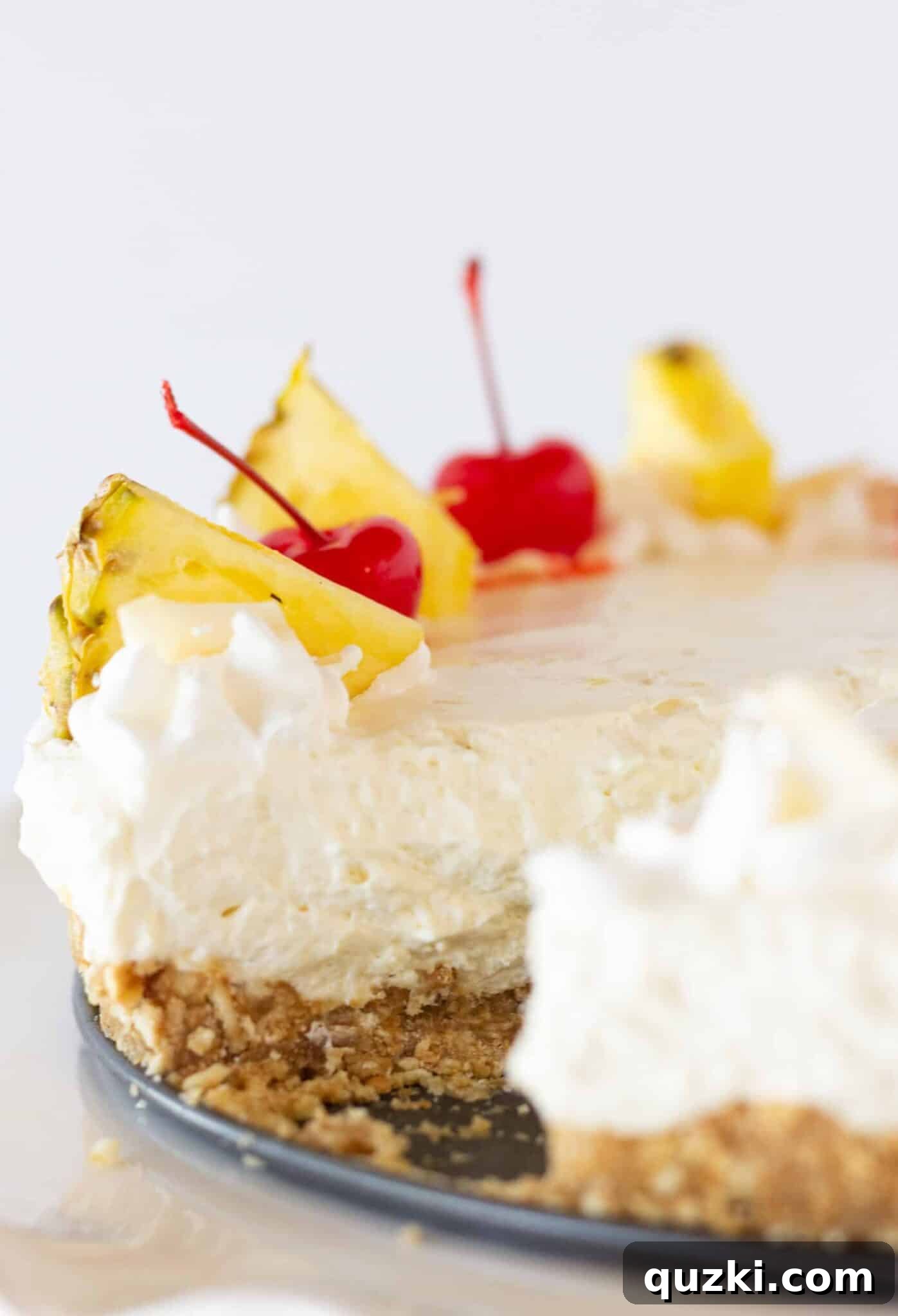 Island Escape No-Bake Cheesecake 3 A freshly cut slice of no-bake Pina Colada cheesecake revealing its creamy texture and vanilla wafer crust, presented on a pristine white plate.