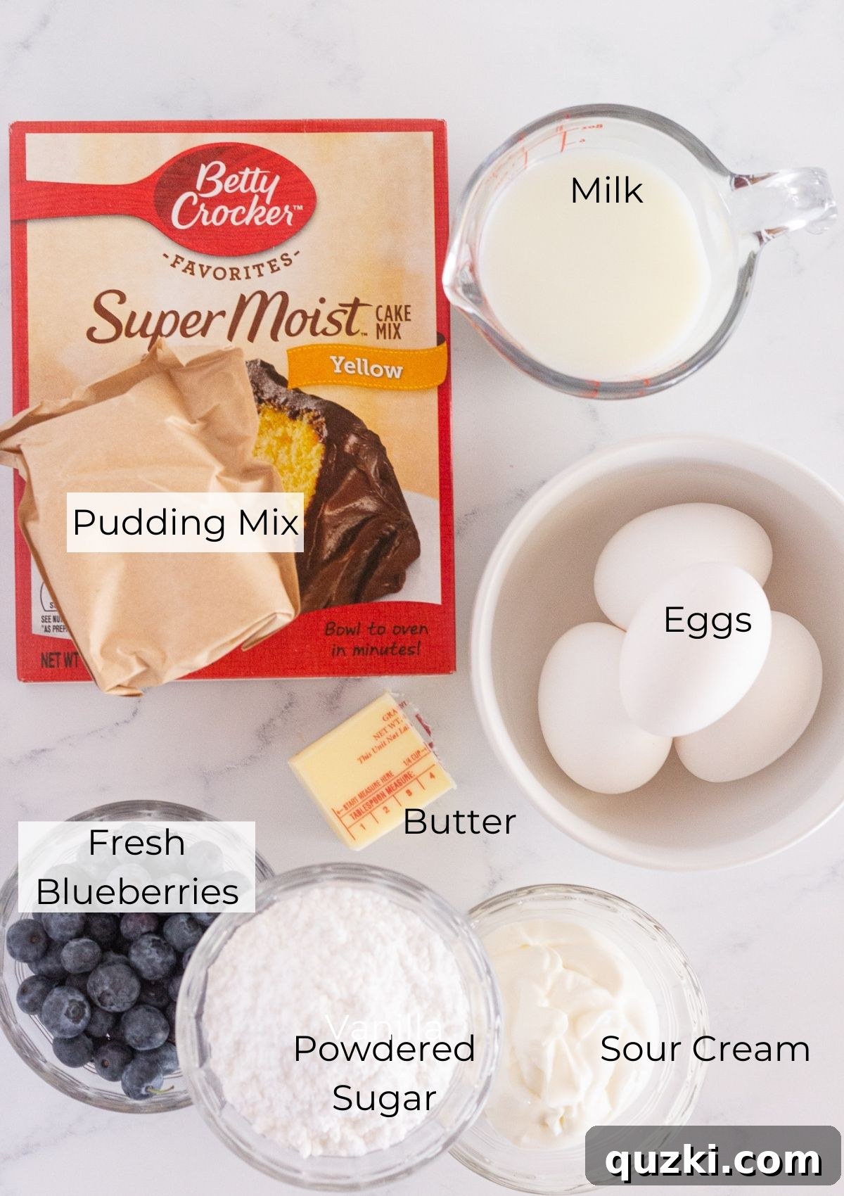 All the necessary ingredients laid out on a clean counter, including a box of cake mix, a box of vanilla pudding, fresh blueberries, eggs, milk, sour cream, and butter, ready for baking.