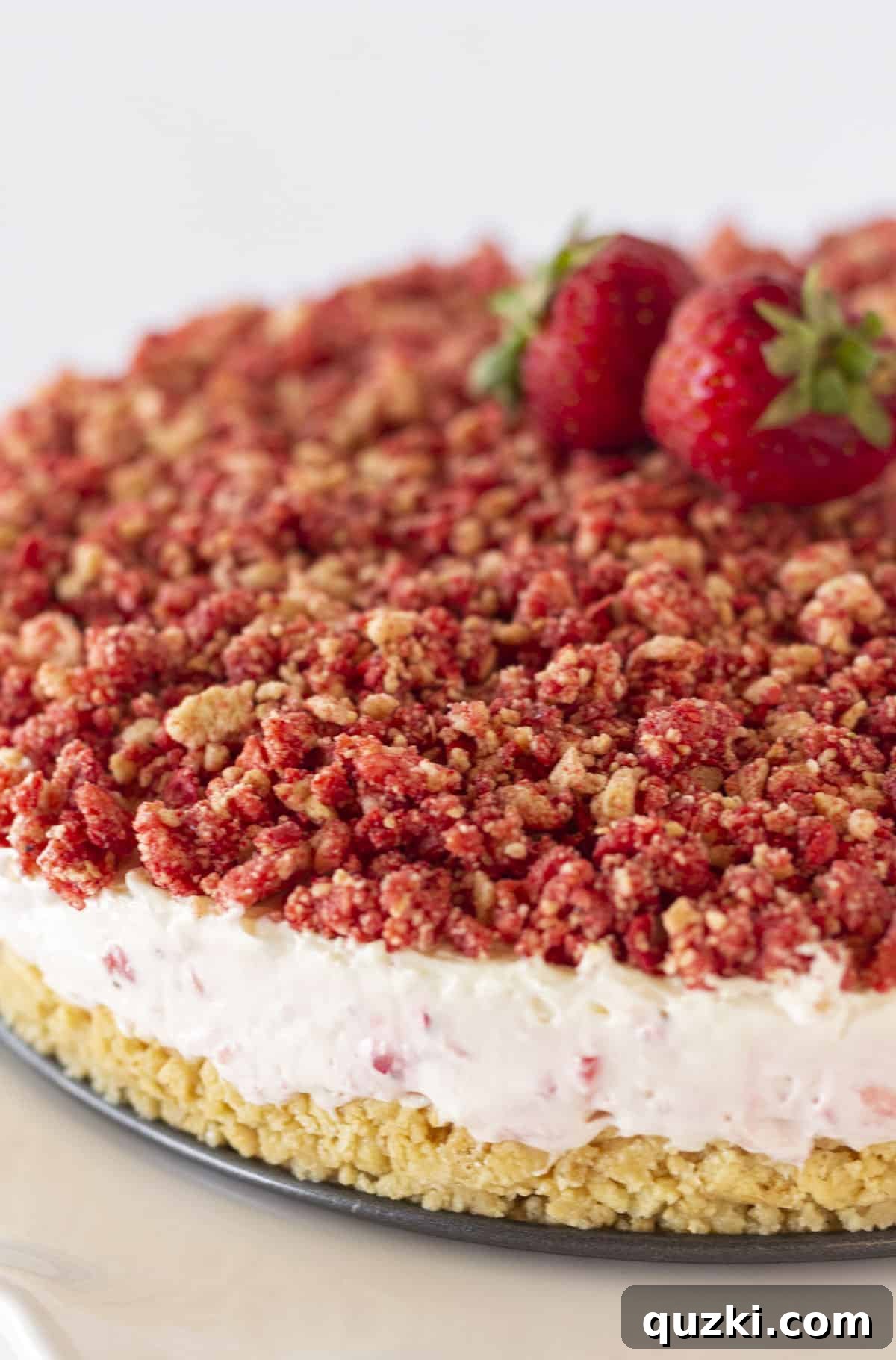 A beautifully decorated whole strawberry crunch cheesecake, garnished with fresh strawberries on top, ready to be served.