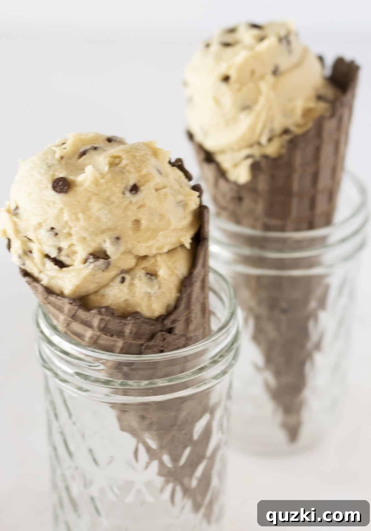 Two chocolate ice cream cones filled with generous scoops of edible eggless cookie dough, ready for a delightful indulgence.