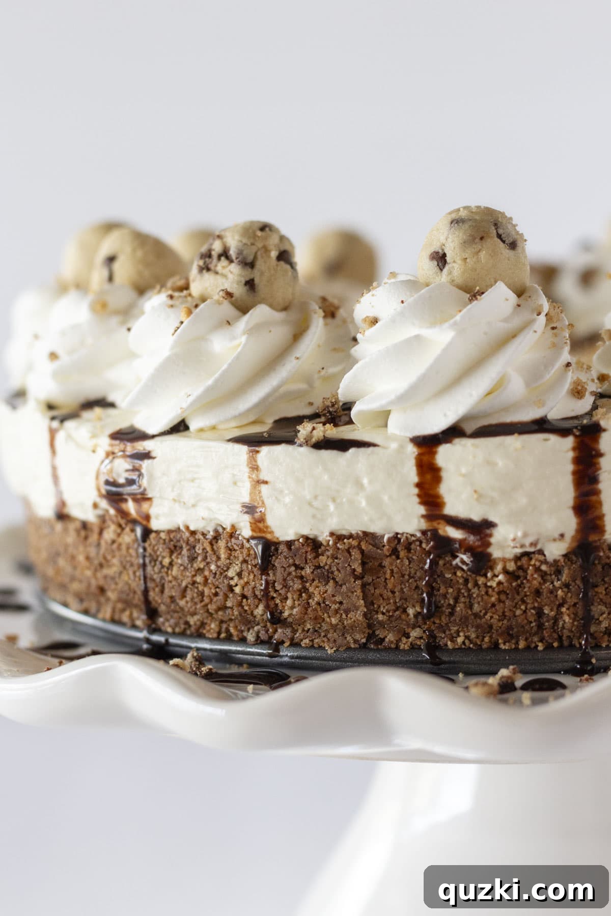 Irresistible No-Bake Cookie Dough Cheesecake 7 A beautifully presented whole no-bake cookie dough cheesecake, garnished with whipped topping rosettes and extra cookie dough balls, ready to be sliced and served.