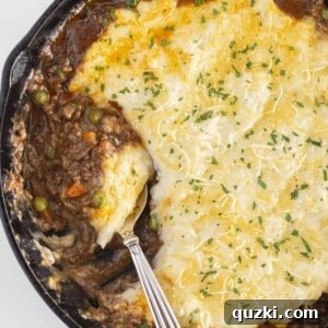 A finished Shepherd's Pie in a cast iron skillet being served with a spoon. The pie features a golden mashed potato topping and a rich meat and vegetable filling.