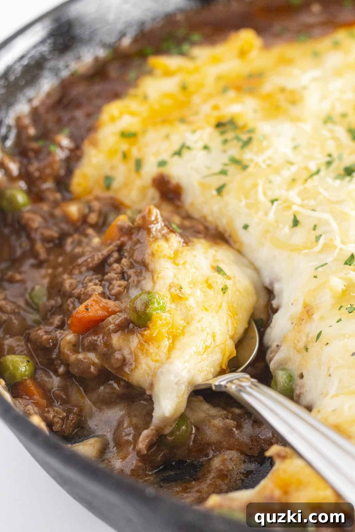 A close up photo of the cast iron shepherd's pie with a spoon in it, ready for serving.