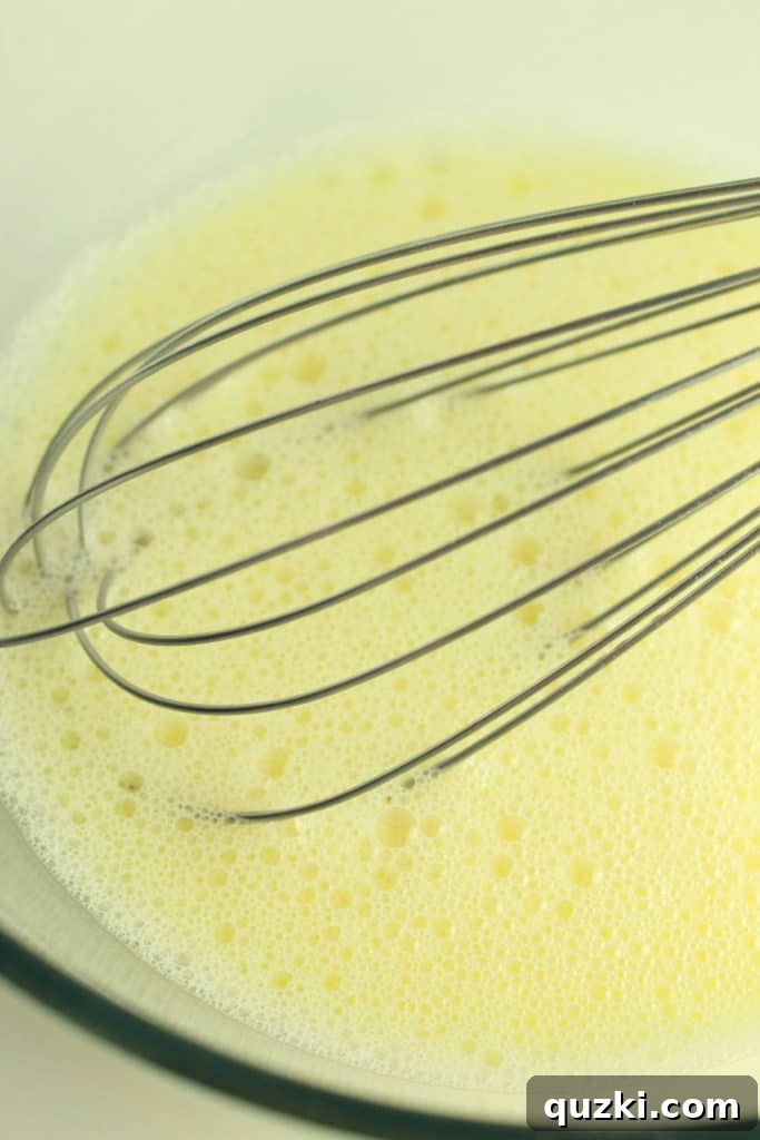 A hand mixing yellow food coloring into pancake batter in a white bowl