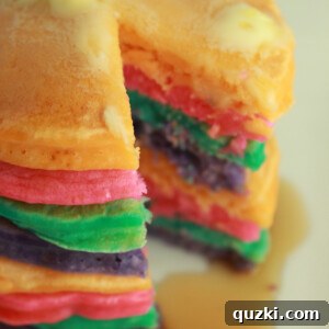 A stack of golden, fluffy rainbow pancakes on a white plate, ready to be enjoyed