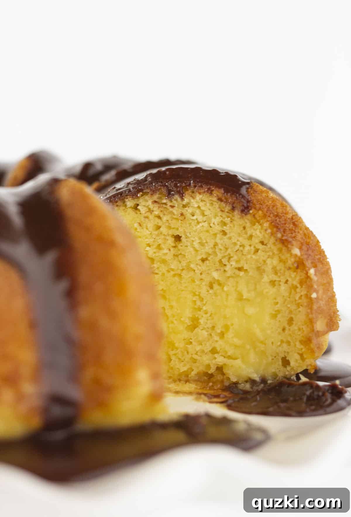 Effortless Boston Cream Pie Poke Cake 8 A close-up view of a slice of Boston Cream Pie Poke cake, revealing the creamy vanilla pudding filling nestled within the golden cake layers, topped with chocolate ganache.