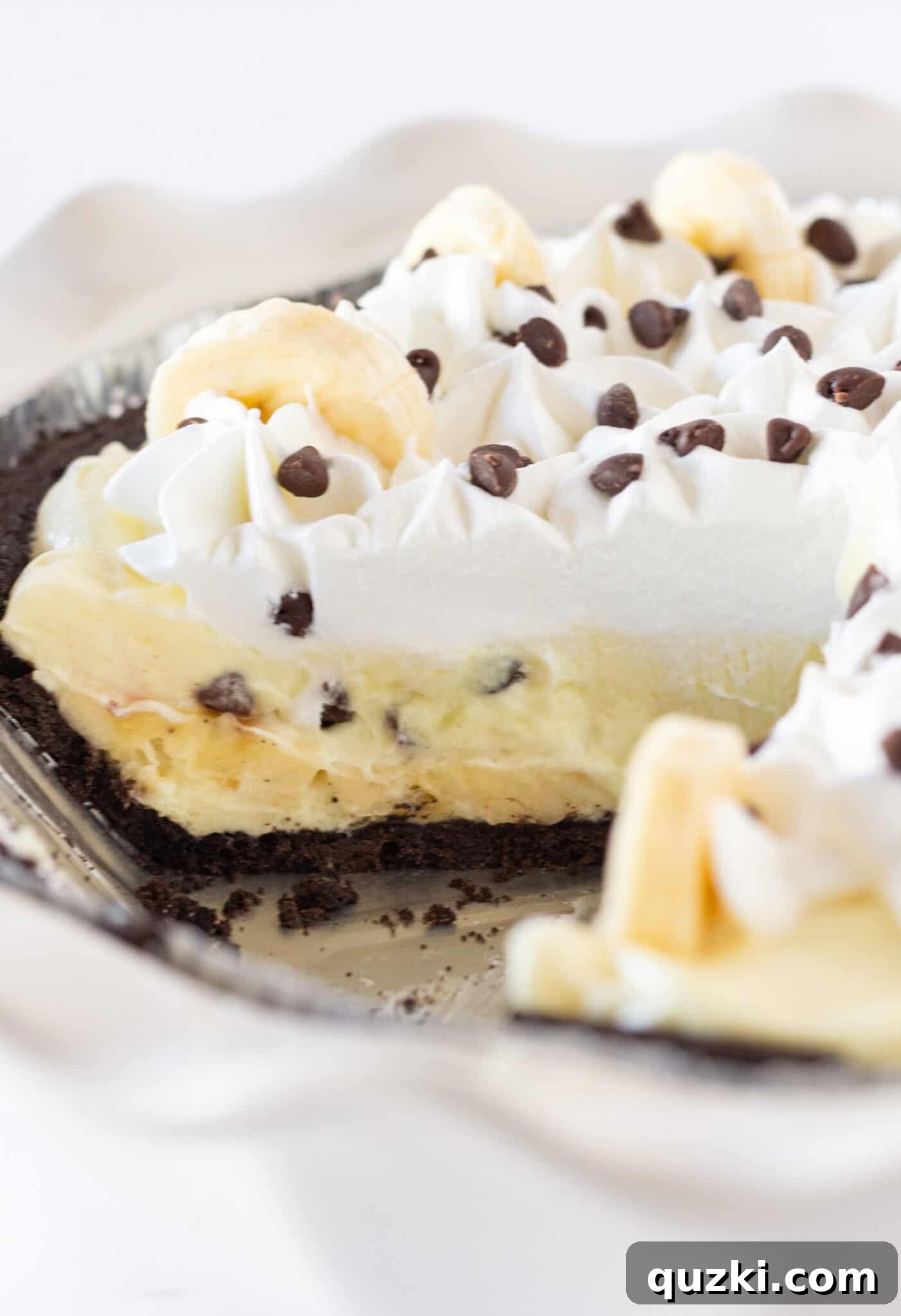 Irresistible Chocolate Chip Banana Cream Pie 3 A close-up view of a slice of Chocolate Chip Banana Cream Pie, showcasing its creamy layers, fresh banana slices, and scattered chocolate chips inside a rich chocolate cookie crust.