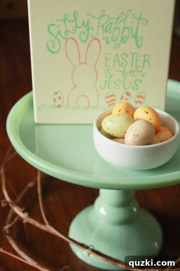 Hop into Easter Decor Ideas 9 A charming pedestal cake plate displaying a rustic wooden Easter sign, a white bowl filled with speckled eggs, and subtle grapevine accents, creating an elegant spring vignette.