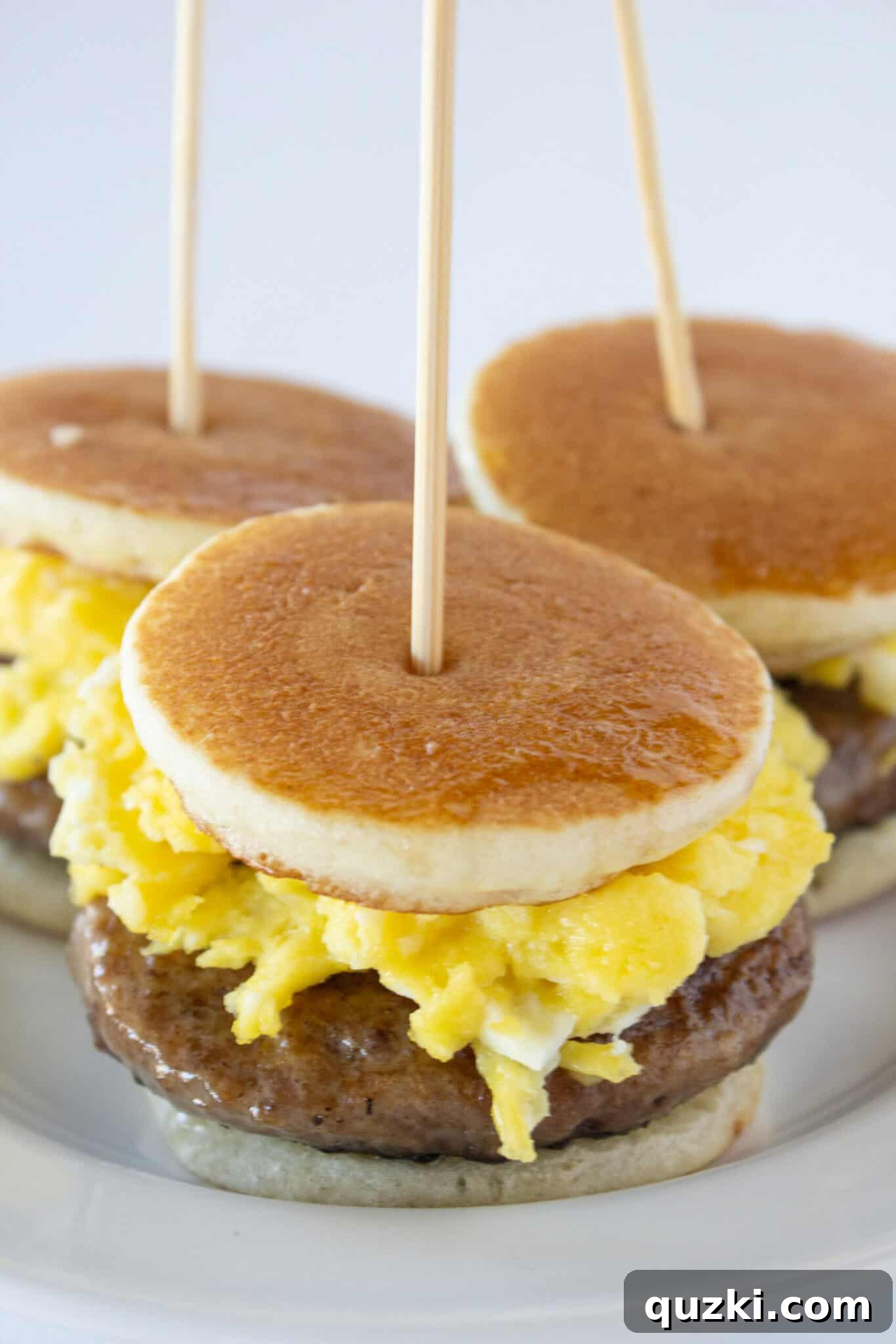 Sweet and Savory Pancake Sausage Egg Sliders 11 Close-up of a single Pancake Sausage and Egg Slider, showing the layers of pancake, sausage, and egg, drizzled with maple syrup