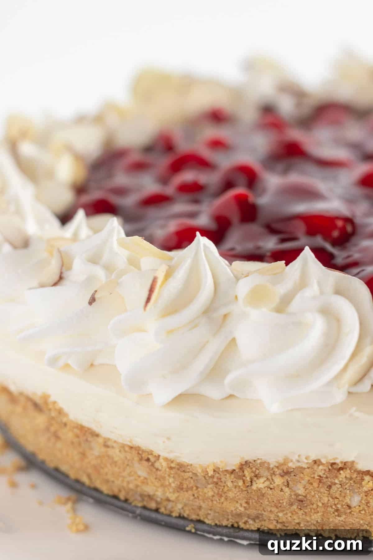 A pristine No-Bake Cherry Cheesecake, beautifully topped with sweet cherry pie filling and delicate almond slices, showcasing its creamy texture and rich graham cracker crust.