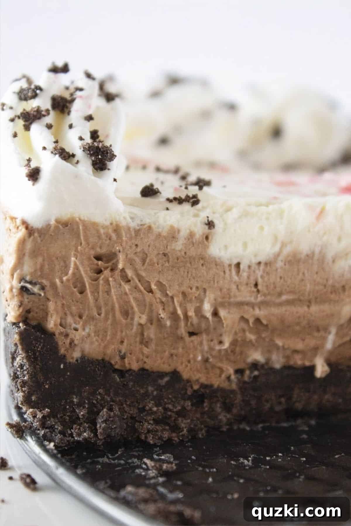 A beautifully layered no-bake chocolate peppermint cheesecake with a rich chocolate crust, topped with crushed candy canes, perfect for a festive Christmas dessert.