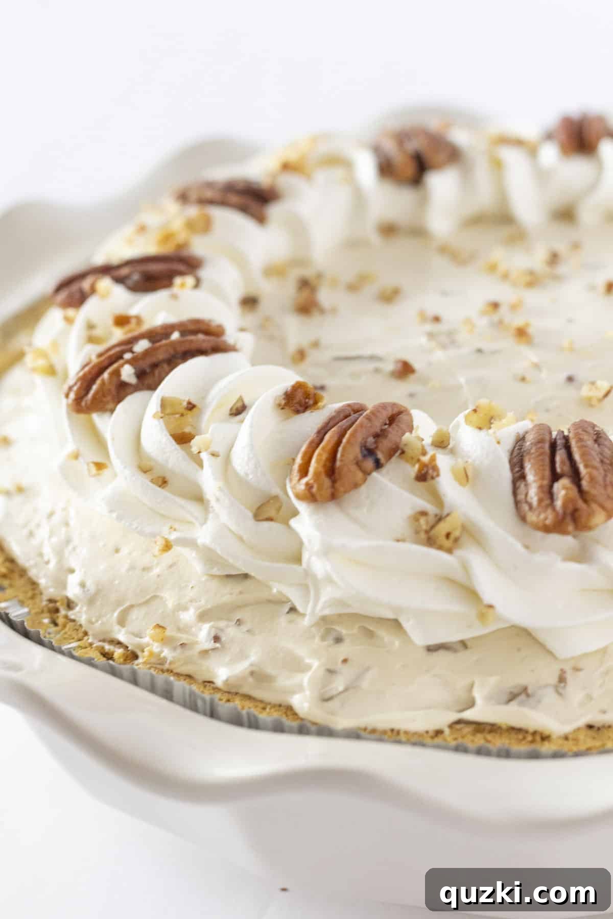 A sumptuous No-Bake Butter Pecan Cream Pie, generously adorned with swirls of whipped cream and a sprinkle of toasted pecans, presented as an elegant holiday dessert.