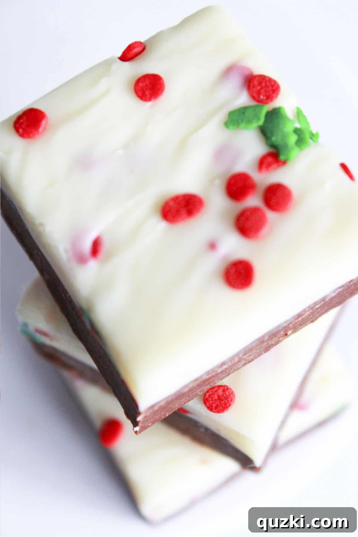 Three delectable pieces of double layer holiday fudge, stacked elegantly, showcasing the distinct layers and topped with festive holly sprinkles for Christmas.