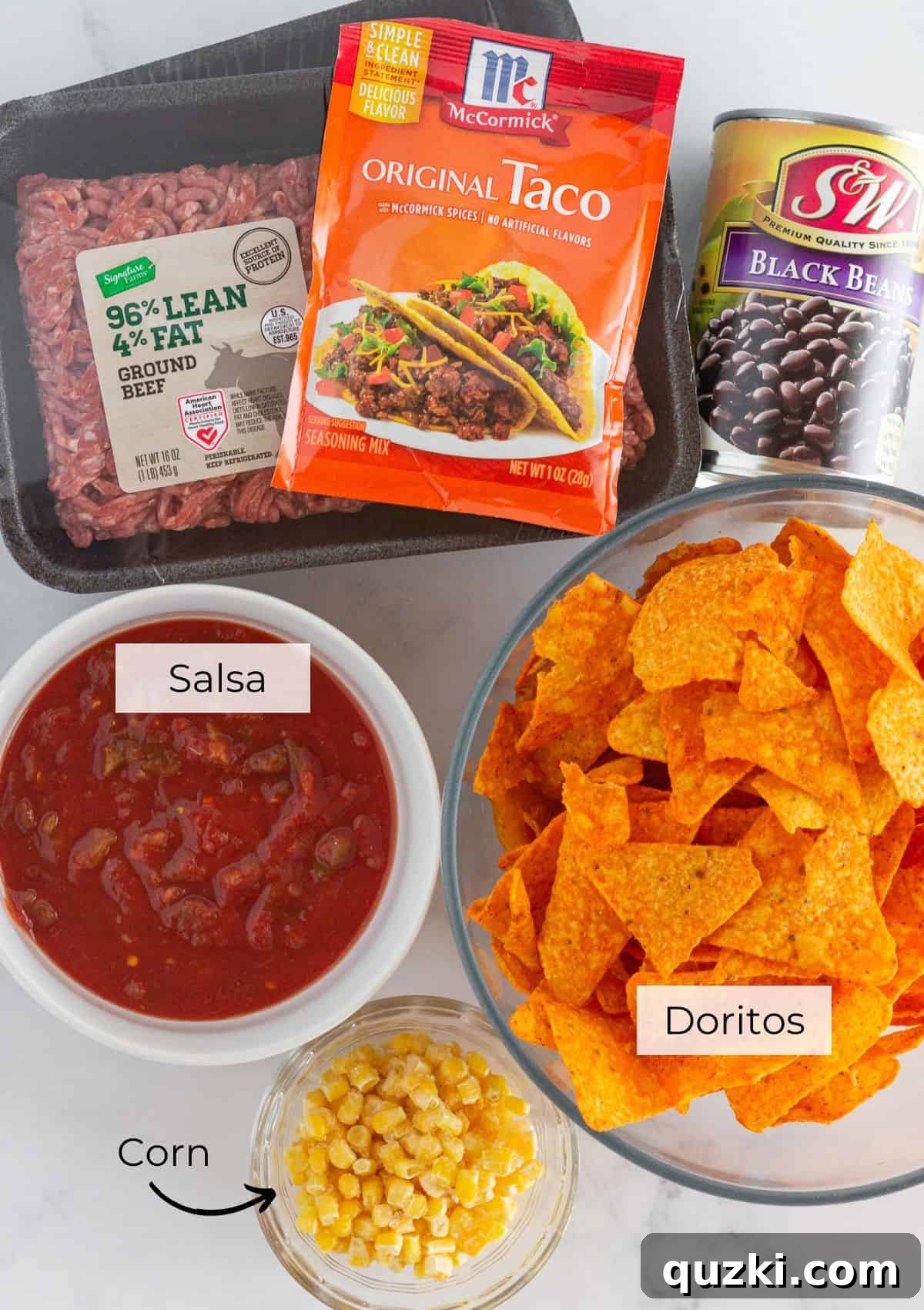 An array of fresh ingredients laid out, including ground beef, corn, black beans, salsa, cheese, and a bag of Doritos, ready for making the casserole.