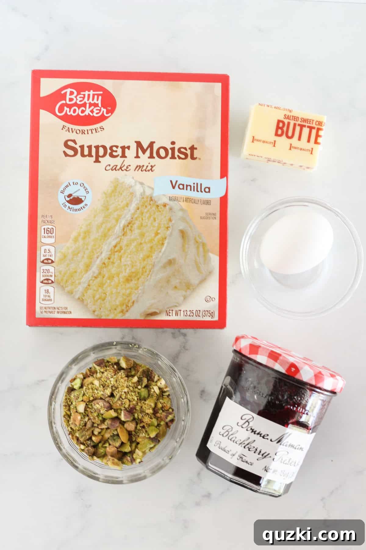 All the fresh ingredients laid out on a table, including vanilla cake mix, butter, egg, blackberry jam, and pistachios, ready to make Blackberry Crumble Bars.