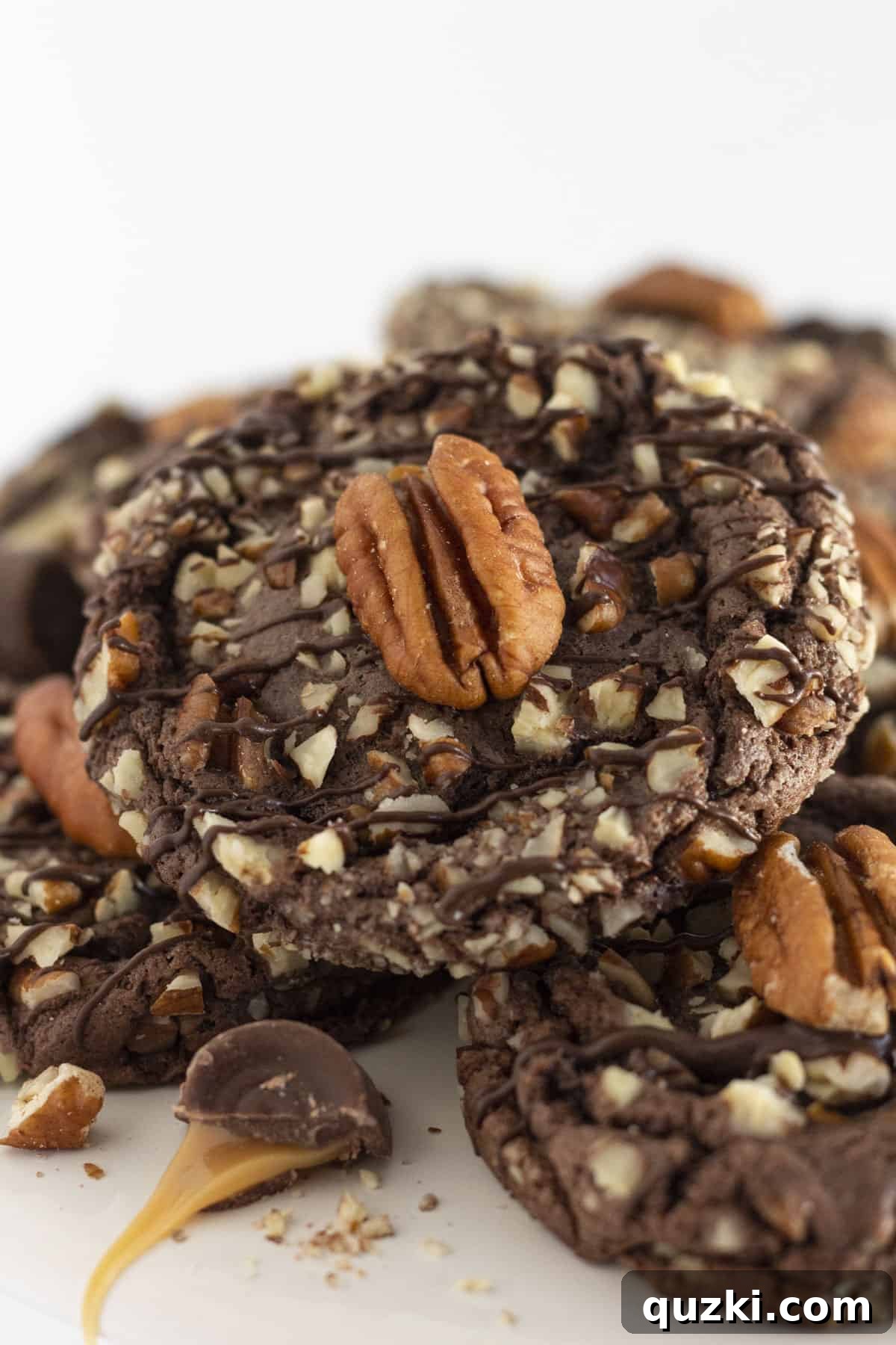 Simple Chocolate Pecan Turtle Cookies 2 Decadent Turtle Cookies arranged on a white cake plate, surrounded by scattered pecans and drizzled caramel.
