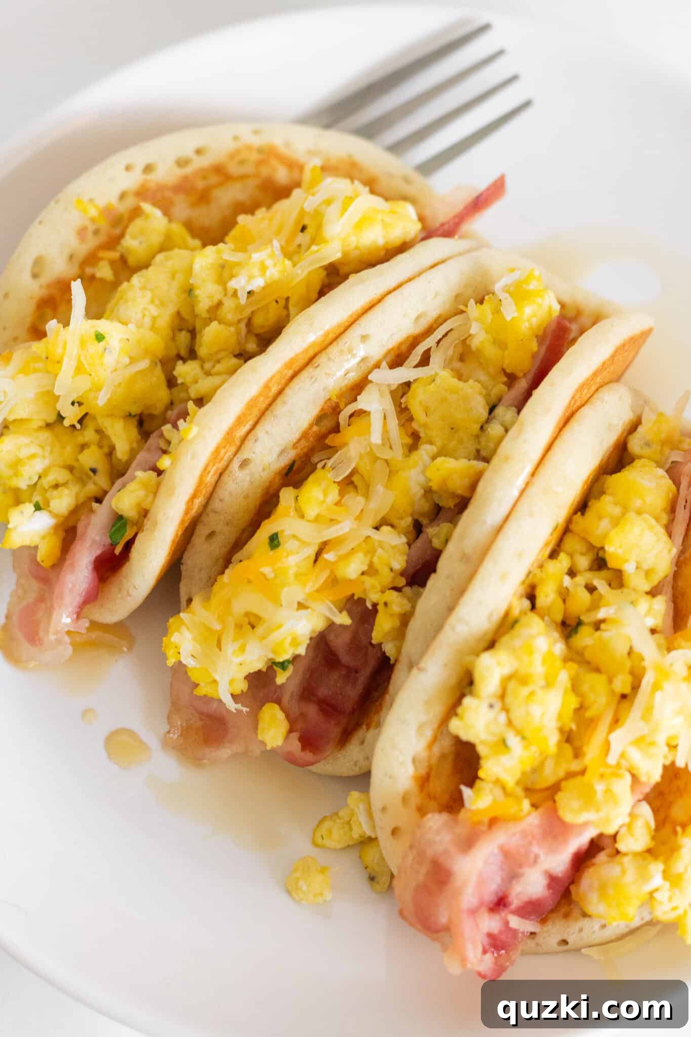 Flapjack Taco Twists 2 A plate featuring two irresistible pancake tacos, generously filled with golden scrambled eggs and perfectly cooked crispy bacon.