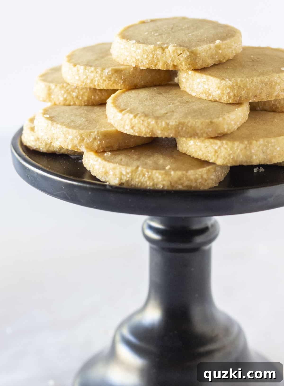 Brown Sugar Shortbread Delight 6 A beautiful display of a dozen golden brown sugar shortbread cookies arranged artfully on a sleek black cake stand.