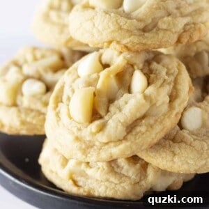 A black cake plate with a dozen of macadamia nut white chocolate chip cookies stacked on top.