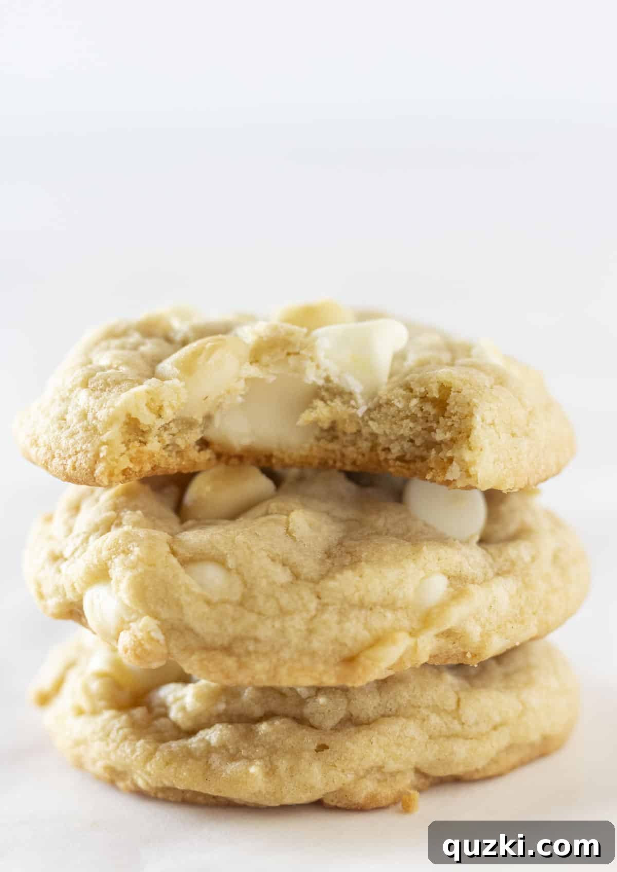Three White Chocolate Macadamia Cookies stacked on top of each other with a bite taken out of the top one.