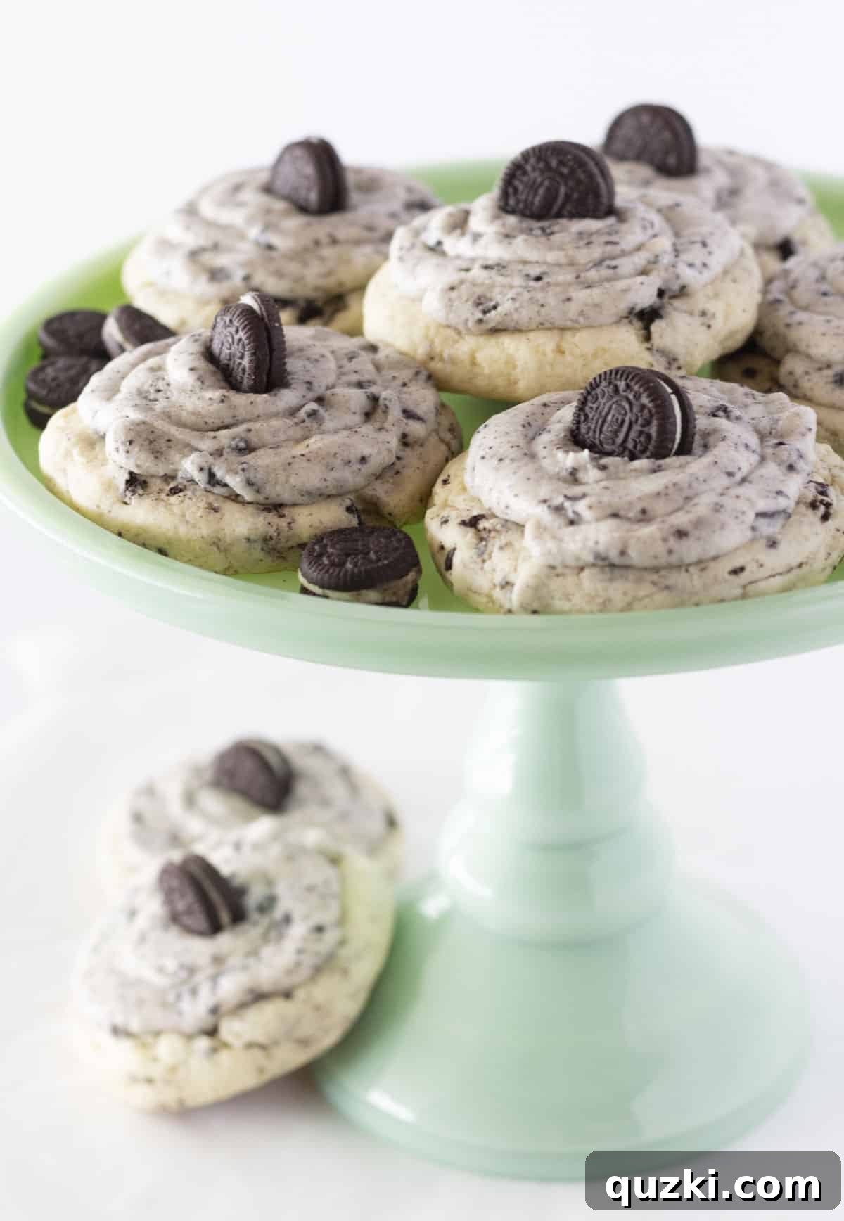 Several large, decadent cookies and cream cookies are beautifully arranged on a vibrant green cake plate, showcasing their generous frosting and mini Oreo topping.