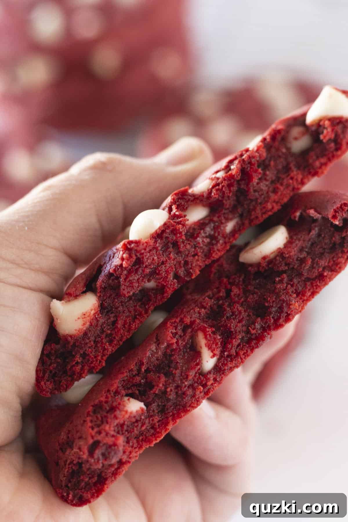 A red velvet cookie with white chocolate chips broken in half, revealing its soft, moist interior.