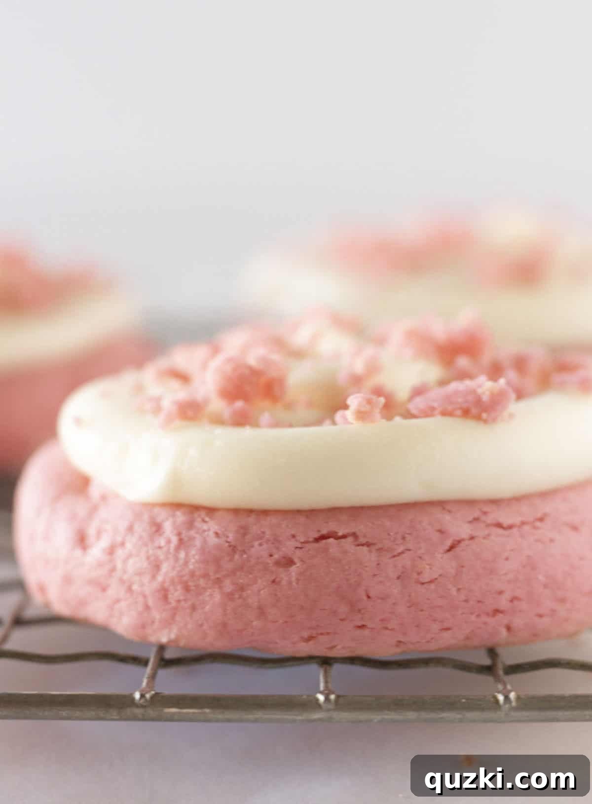 A close up of frosted pink velvet cookies with cookie crumbs on top.