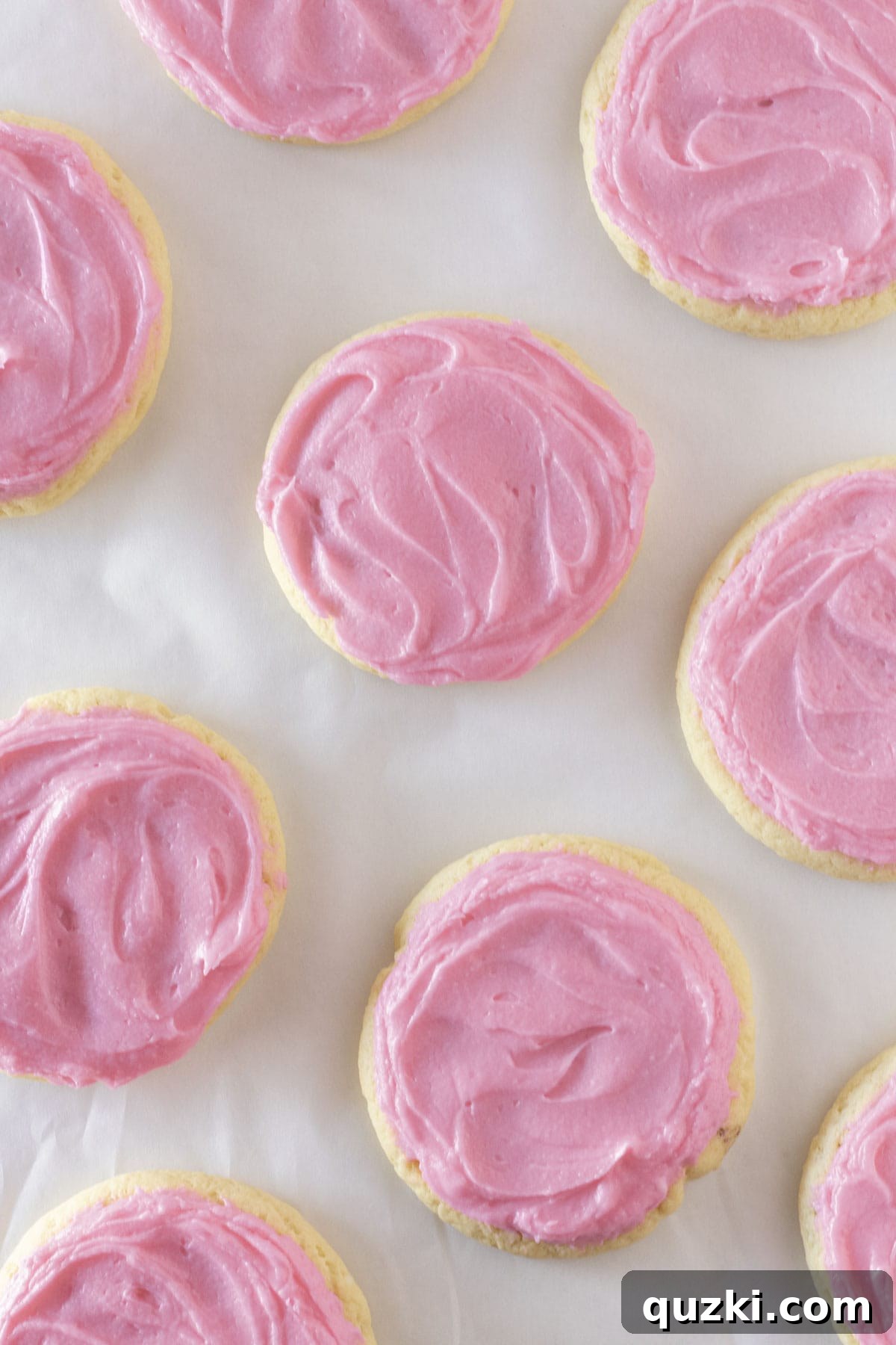 Overhead view of chilled sugar cookies with pink frosting on a white surface.