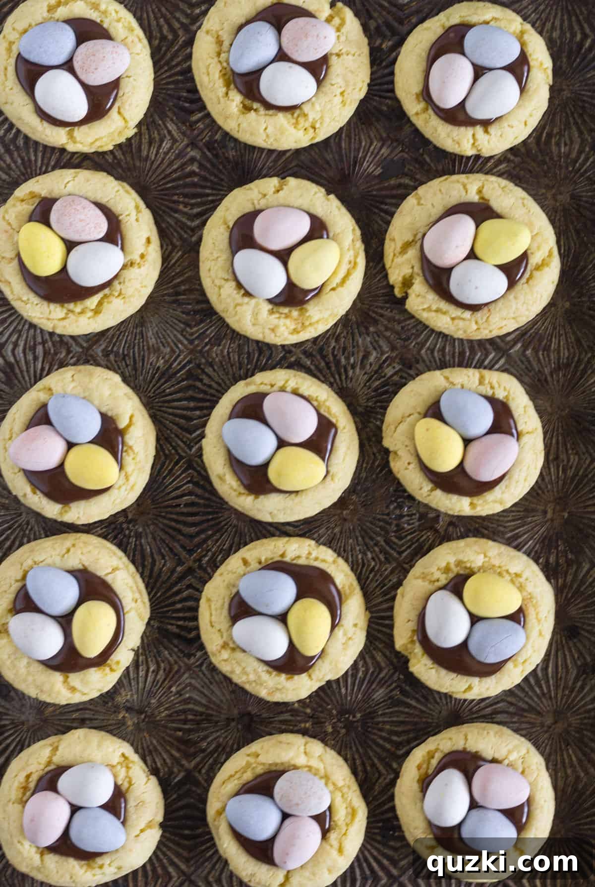 Quick-Bake Cadbury Mini Egg Cookies 7 Fifteen vibrant Cadbury Mini Egg Cookies neatly arranged on a white cookie sheet, each with a chocolate ganache center adorned with colorful mini eggs.