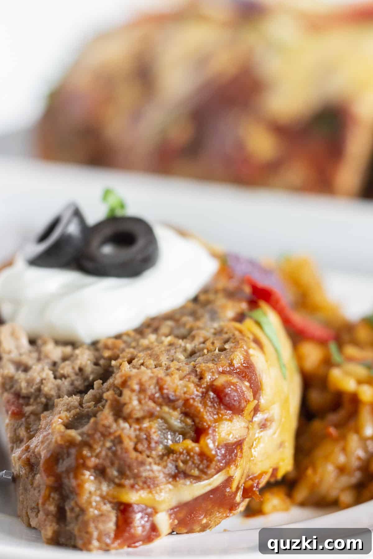 A slice of taco meatloaf with sour cream and olives on top, ready to be served.