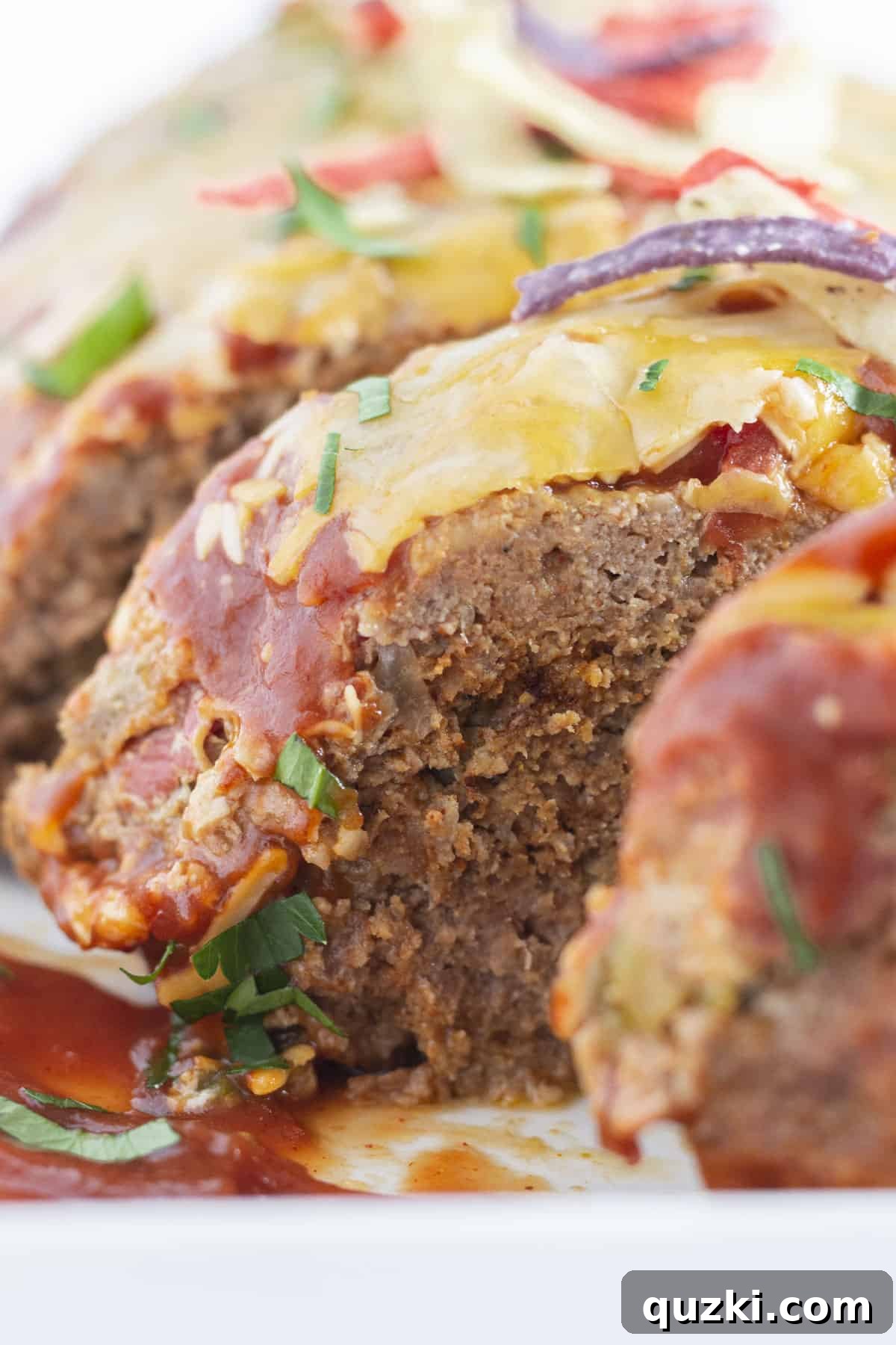 A cooked taco meatloaf that is sliced and topped with tortilla strips and cilantro.
