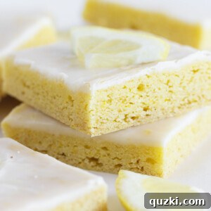A stack of golden, glazed lemon cake mix cookie bars on a white serving tray, garnished with fresh lemon zest.