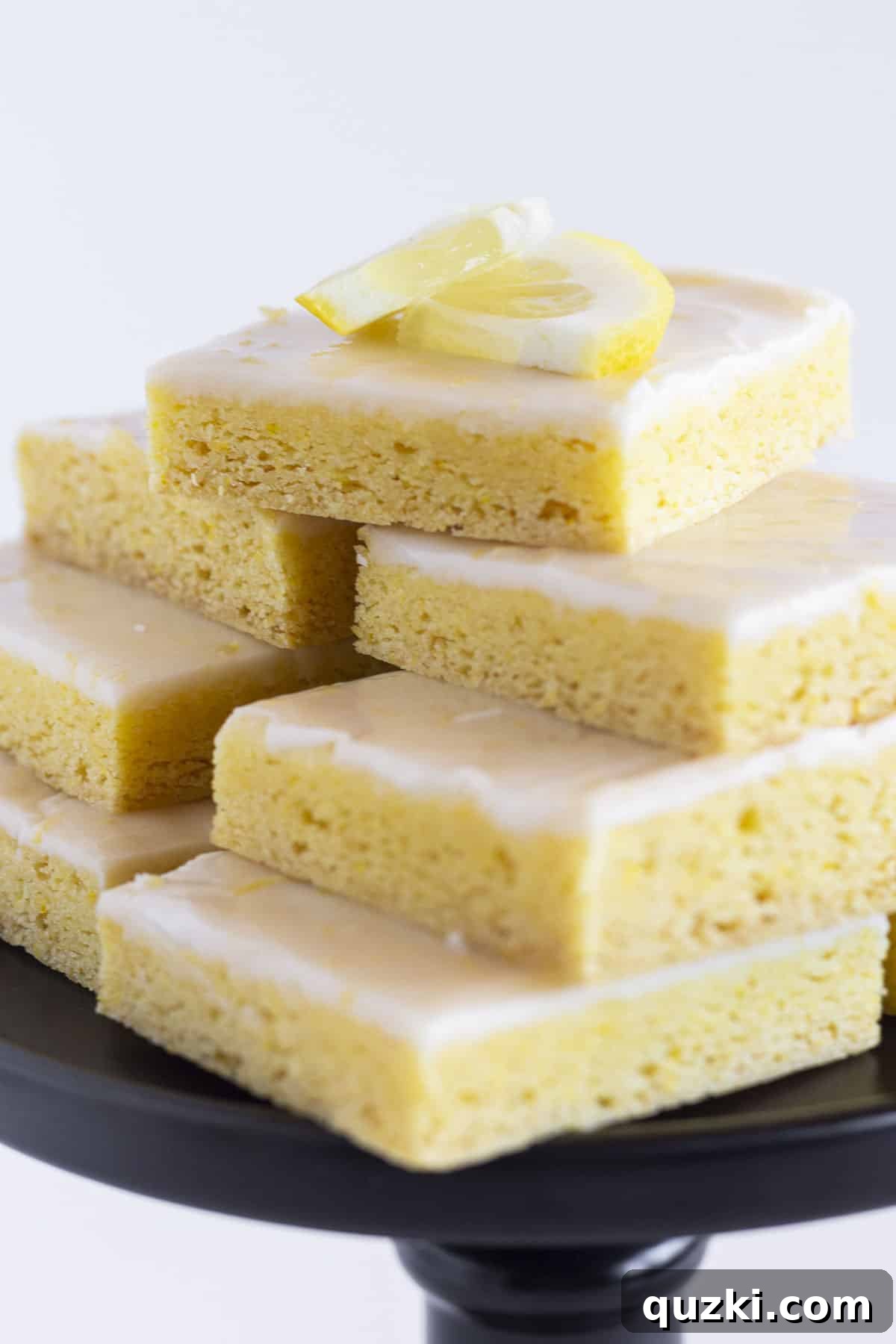 A dozen perfectly cut lemon cake mix cookie bars arranged on an elegant black cake plate, ready for serving.