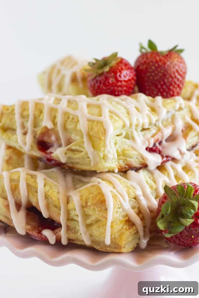 Effortless Strawberry Puff Pastry Delights 2 Fresh strawberry turnovers on a pink cake plate.