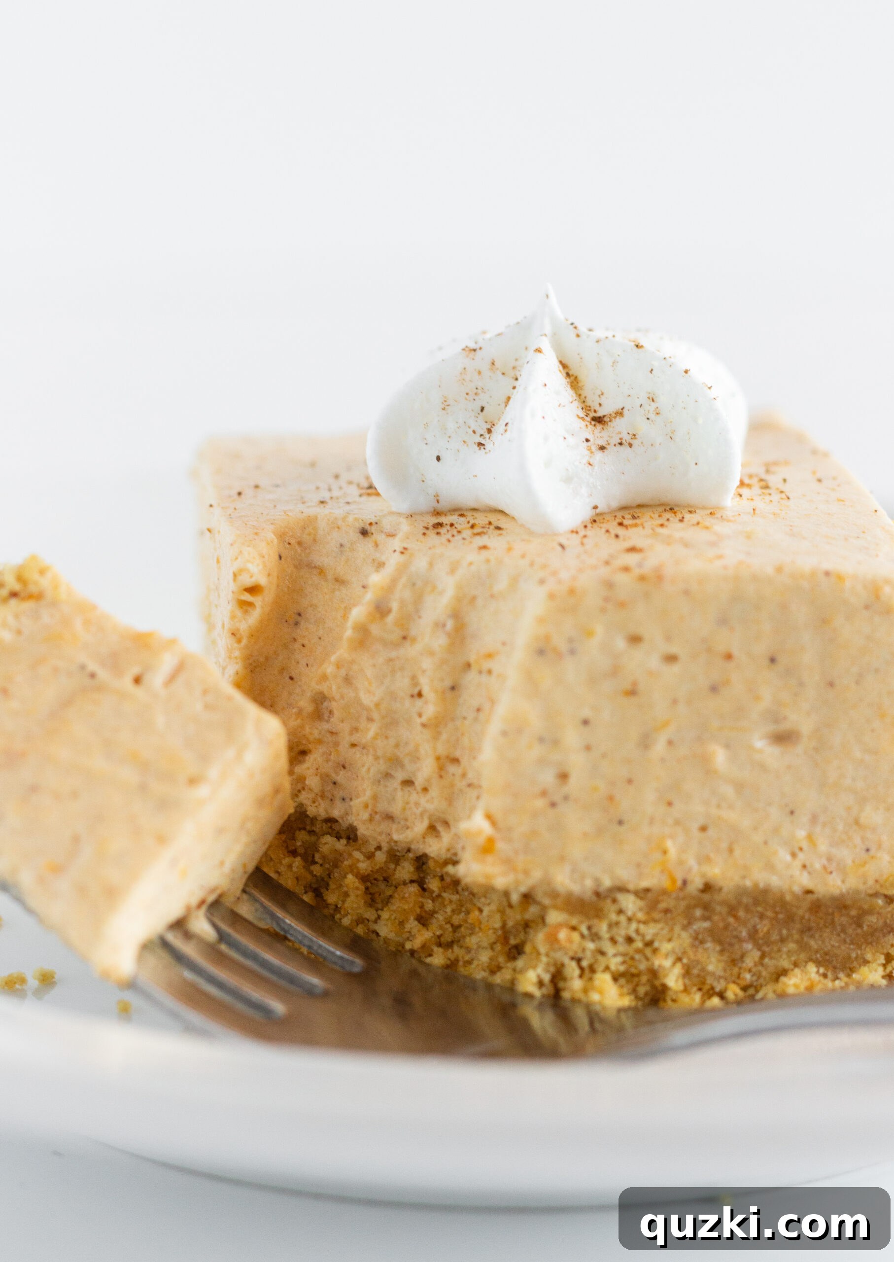 Five No Bake Pumpkin Cheesecake Bars stacked on a white plate, garnished with whipped cream and cinnamon