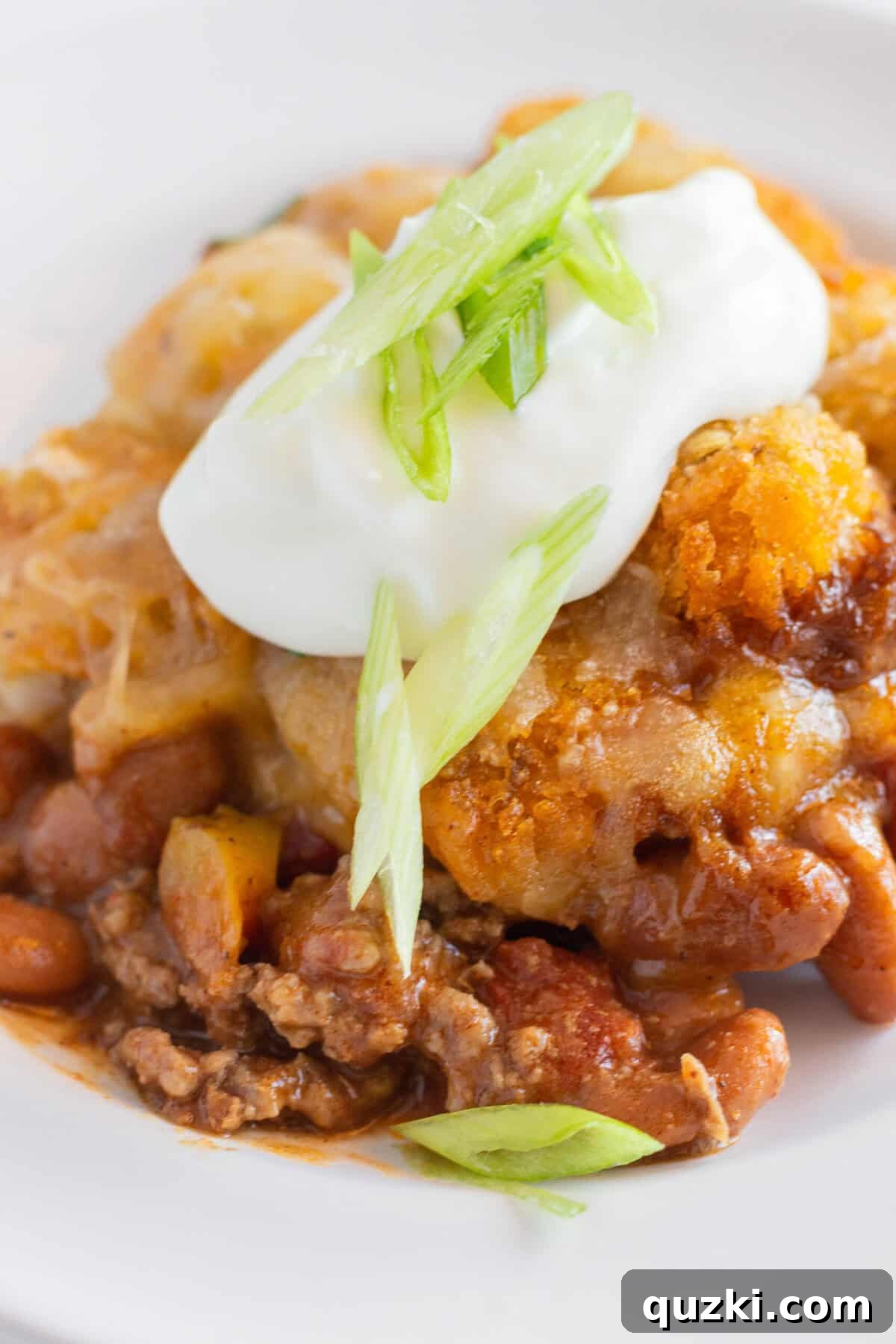 Hearty Chili Tater Tot Bake 2 A single serving of Chili Tater Tot Casserole with sour cream and green onion toppings.