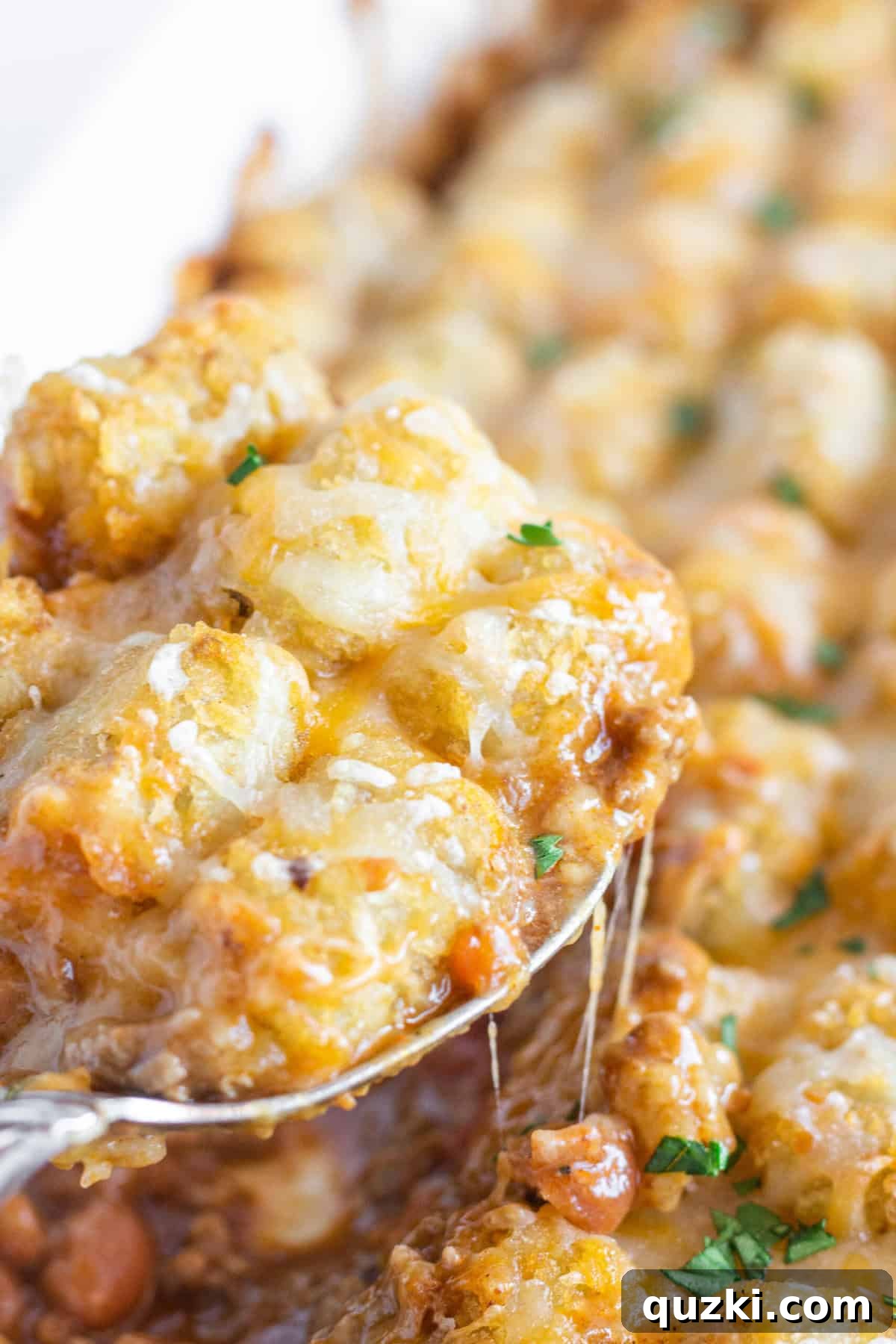 Hearty Chili Tater Tot Bake 6 A spoon serving a helping of Chili Tater Tot Casserole with cheese pulling from the pan.