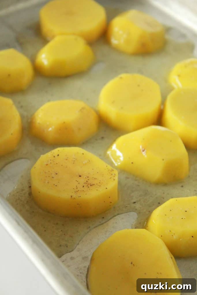 Melt-in-Your-Mouth Roasted Potatoes 5 Seasoned potato slices placed in a single layer within a metal baking dish, ready for the initial roast.