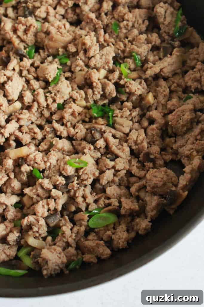 Vibrant Asian Turkey Lettuce Bites 5 Ground turkey browning in a skillet with chopped mushrooms and sliced green onions added, creating a savory and aromatic filling for Asian Lettuce Wraps. Illustrates a key cooking step.