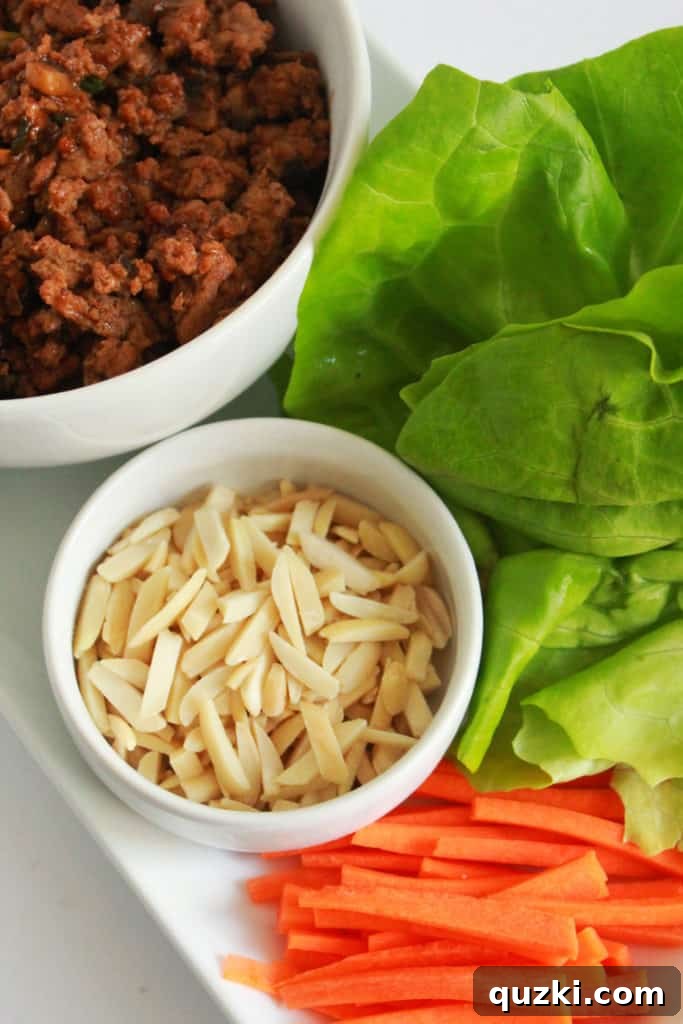 Vibrant Asian Turkey Lettuce Bites 7 Ingredients for assembling Asian Turkey Lettuce Wraps displayed on a table: butter lettuce leaves, a bowl of savory ground turkey filling, matchstick carrots, and slivered almonds. Highlights fresh and colorful components for a healthy meal.