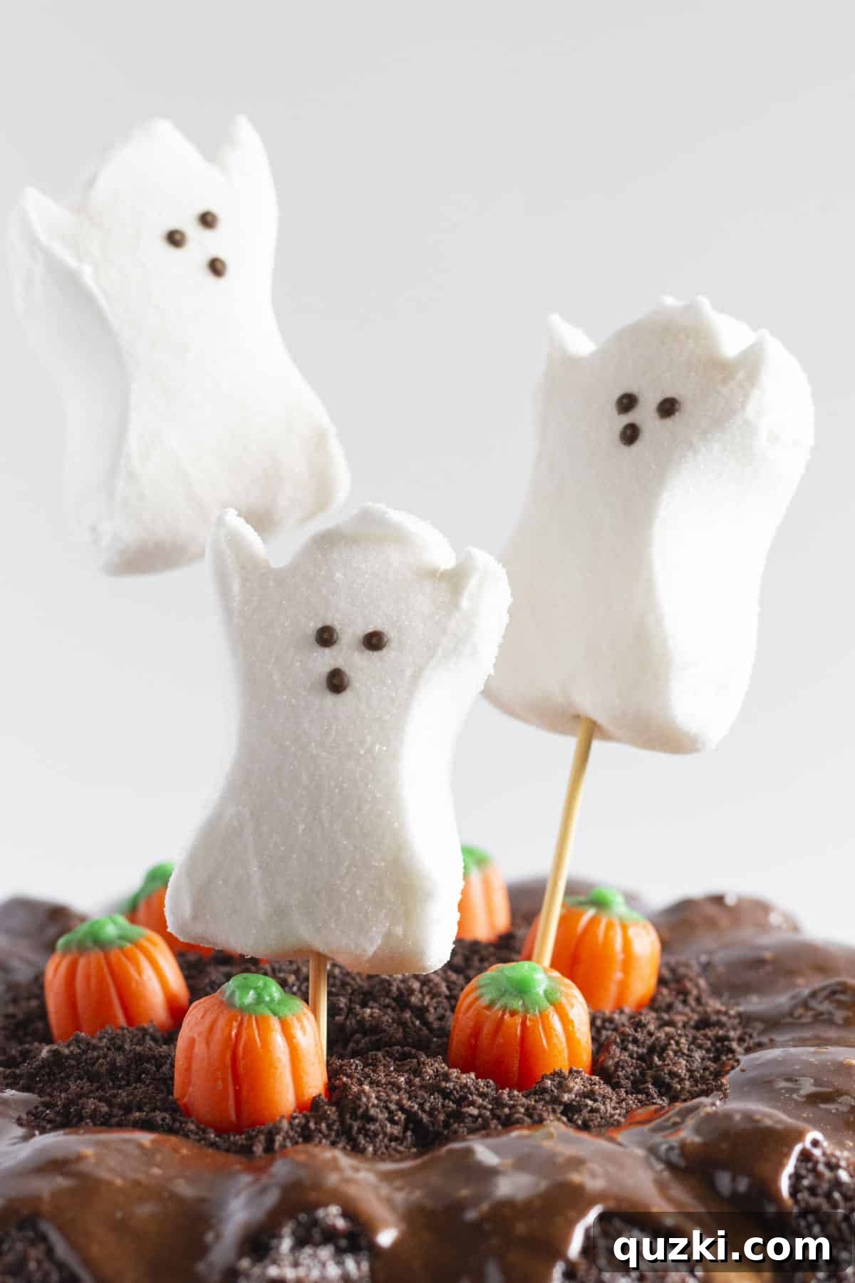 An intricate close-up shot of the Halloween decorations on the bundt cake, showcasing the detailed texture of the Oreo crumbs, the playful marshmallow ghosts, and the festive candy pumpkins.