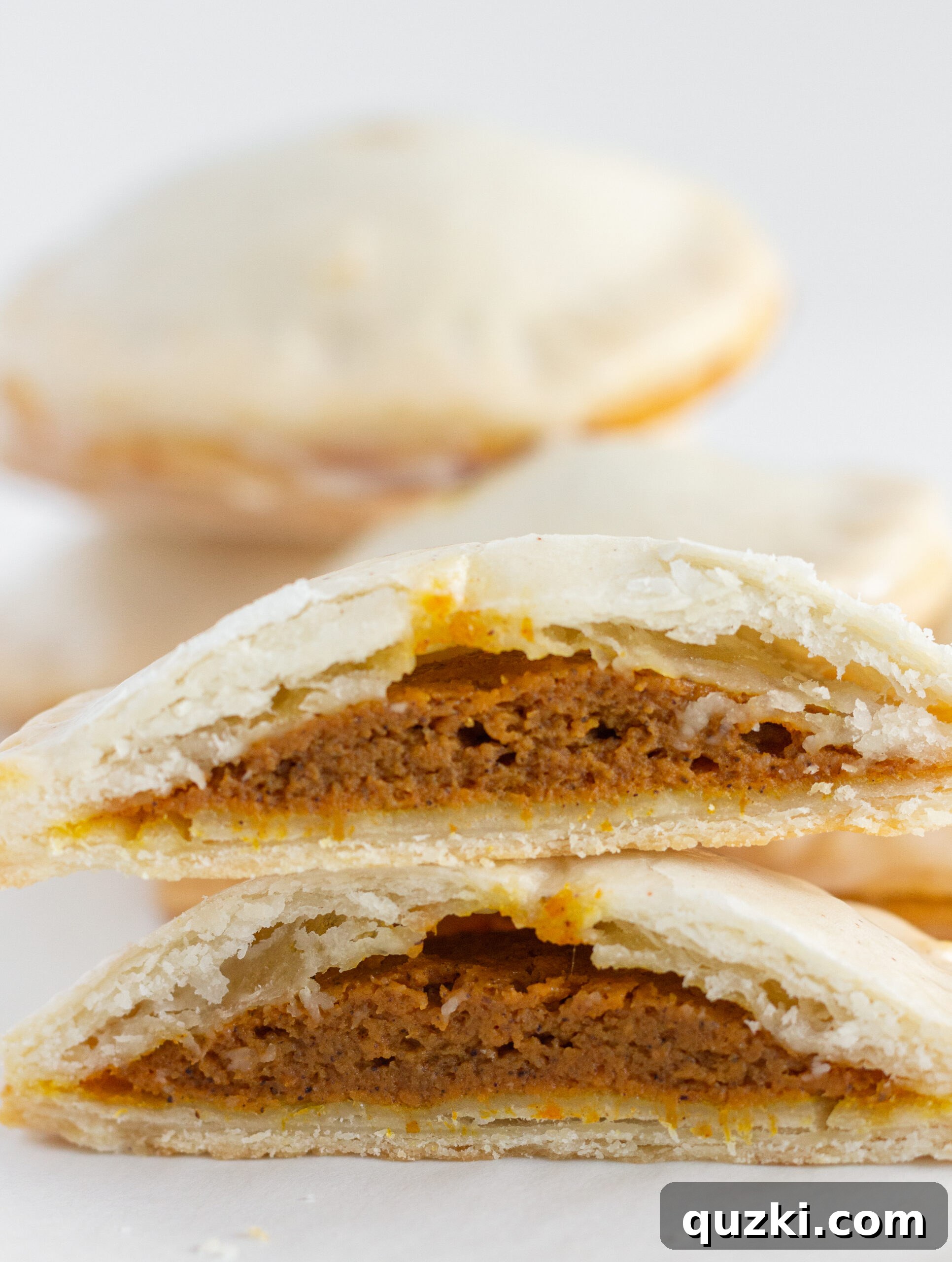 Stacks of golden-brown Easy Pumpkin Hand Pies with one cut open to reveal the creamy, spiced pumpkin pie filling inside, demonstrating its delicious texture.