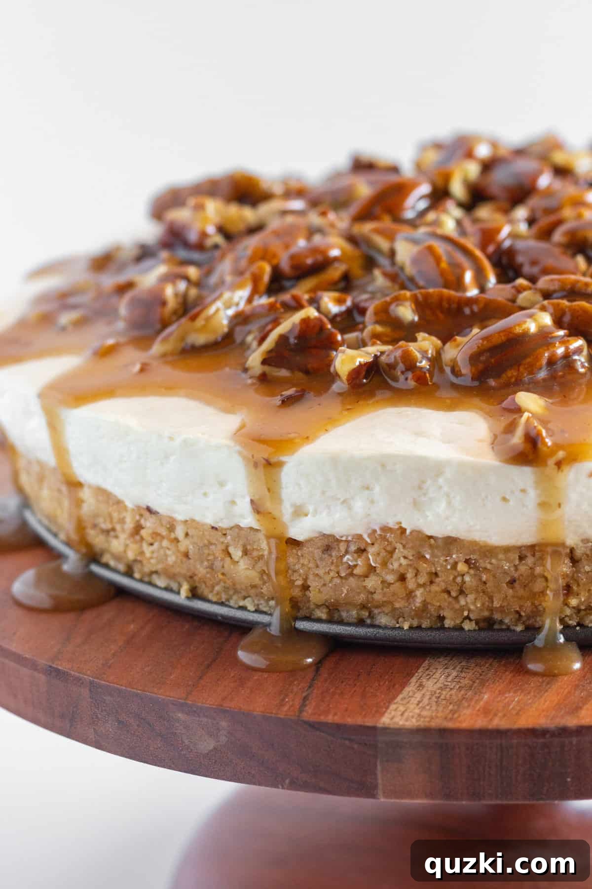 A whole Pecan Pie No Bake Cheesecake on a wood serving plate with the pecan topping dripping onto the plate.