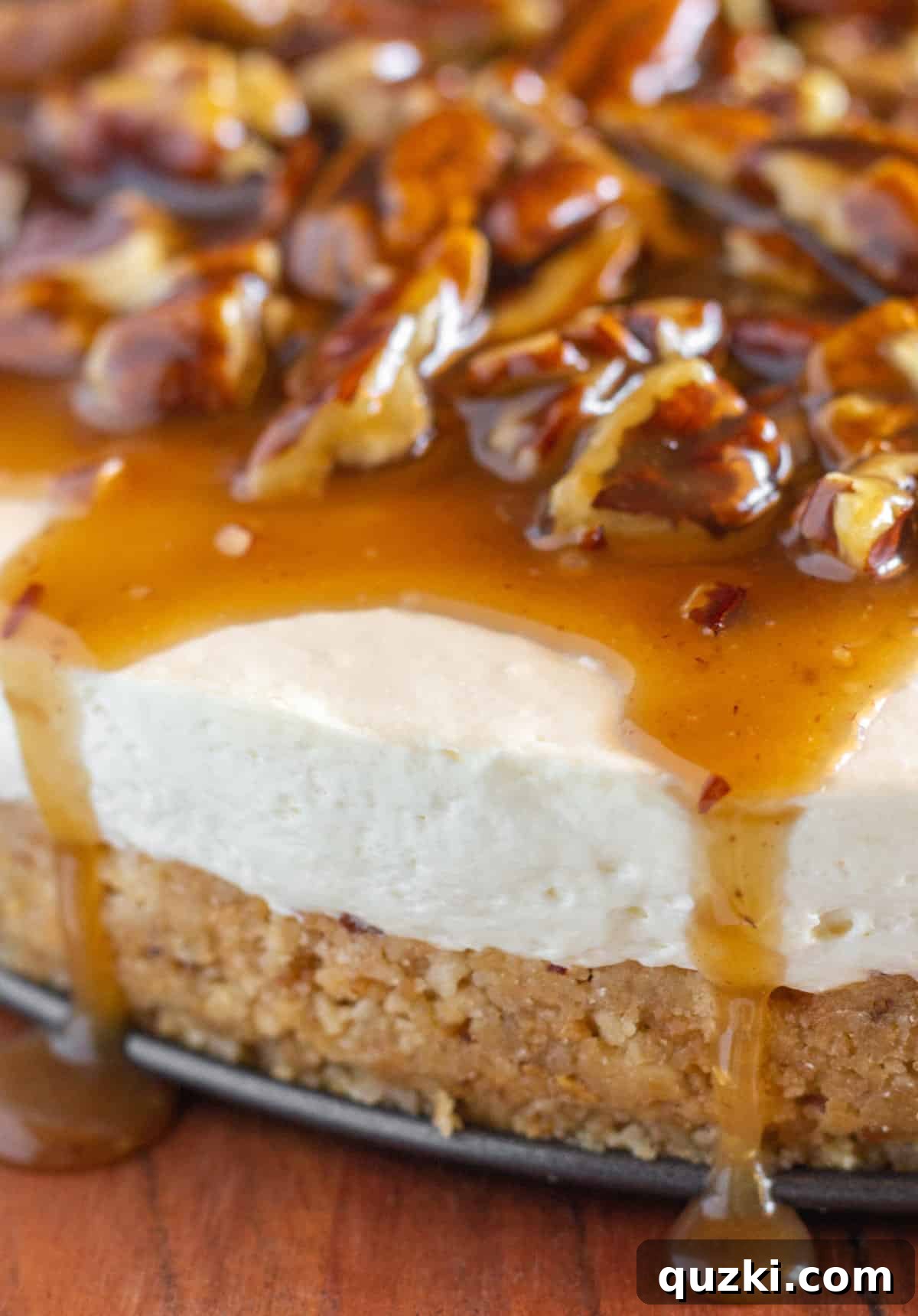 A close up view of a creamy cheesecake with pecan pie topping that is dripping over the edge of the cheesecake.