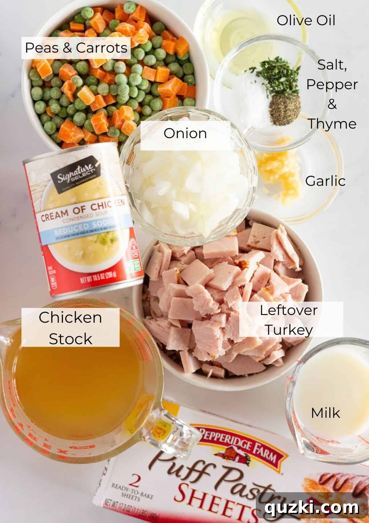 A flat lay of all the ingredients needed to make a homemade leftover turkey pot pie: olive oil, diced onion, minced garlic, cooked turkey, cream of chicken soup, frozen peas and carrots, milk, chicken broth, salt, pepper, fresh thyme, and puff pastry.