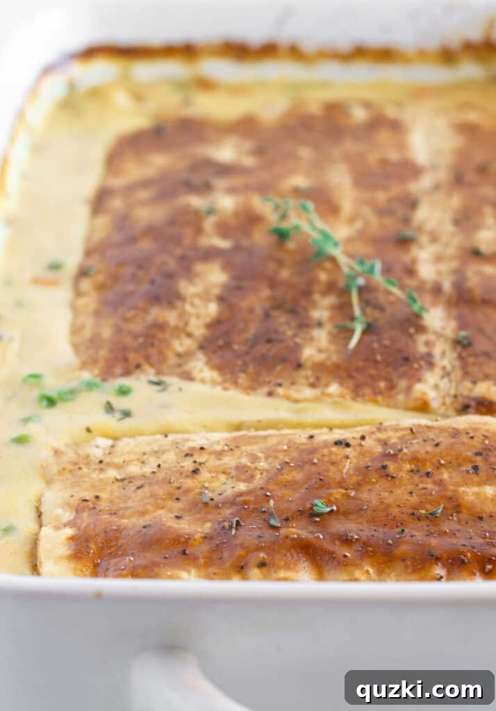 Close-up of a serving of turkey pot pie with puff pastry in a white baking dish, garnished with fresh thyme leaves.