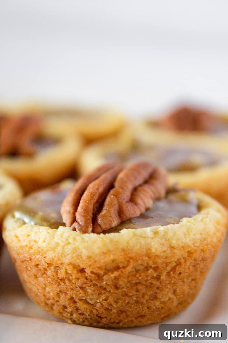 A charming plate adorned with several Pecan Pie Cookie Cups, each perfectly topped with a whole pecan half, inviting you to take a bite.